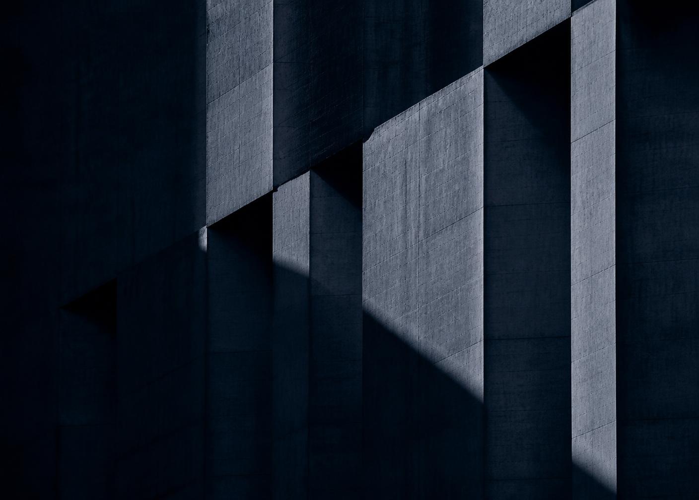 Deep navy concrete facade with strong diagonal shadow across stepped structural planes
